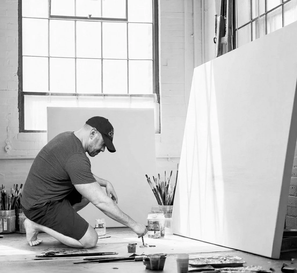 Adam Cooley working in his studio, kneeling on the floor while painting on large canvas panels.