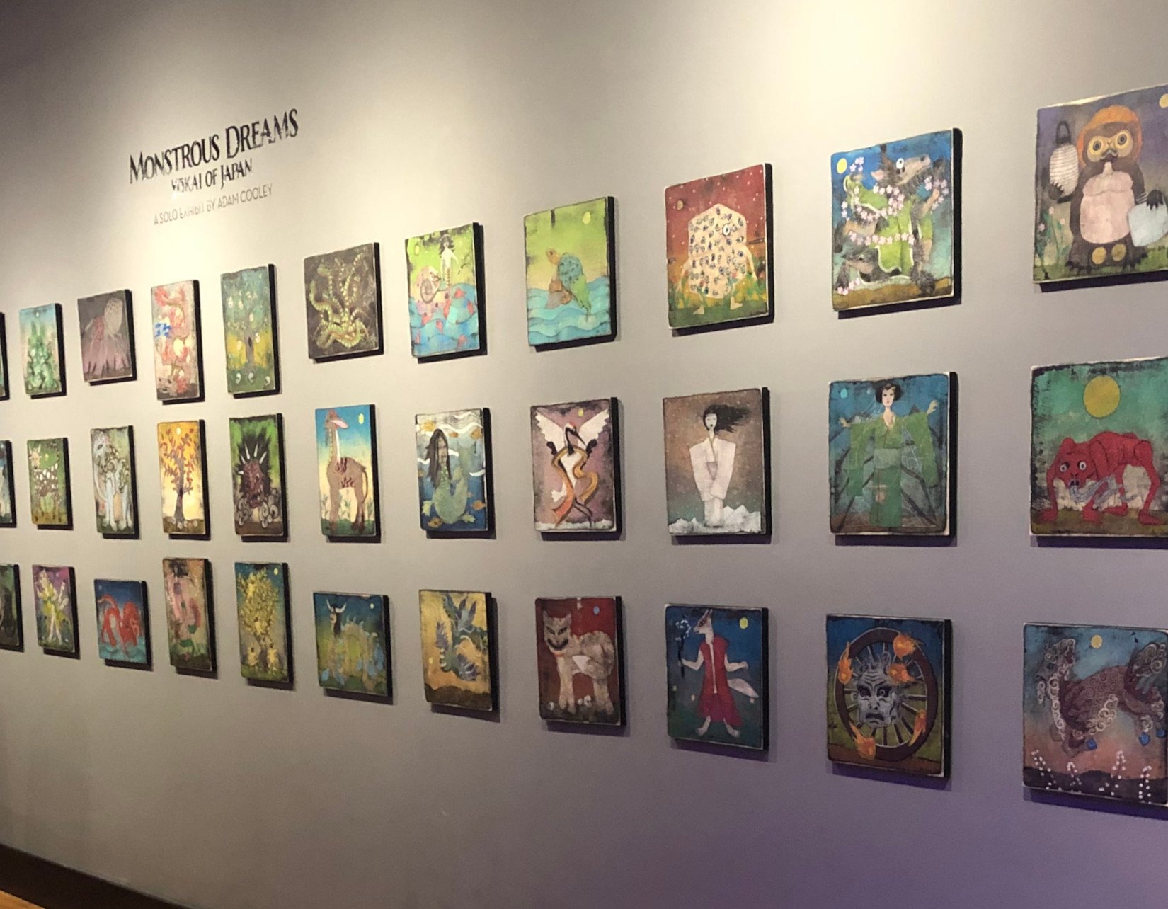 Installation view of Adam Cooley paintings featuring colorful fantasy creatures, animals, and Japanese yokai displayed in a gallery.