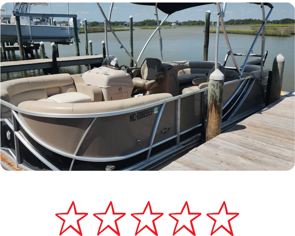 A pontoon boat is docked at a wooden pier on a calm body of water with grassy marshlands and a clear sky in the background.