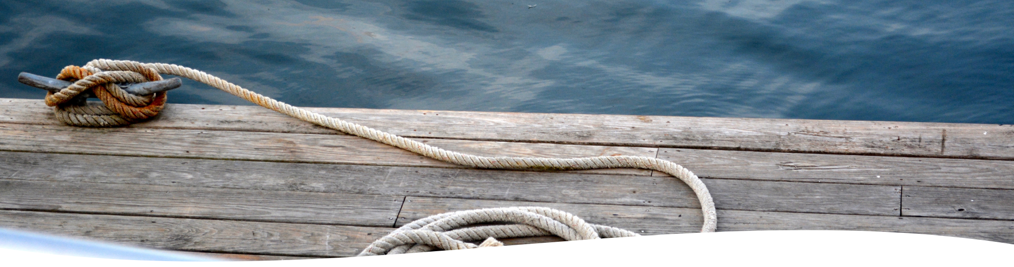 A wooden dock with a thick rope tied around a metal cleat, extending over the water.