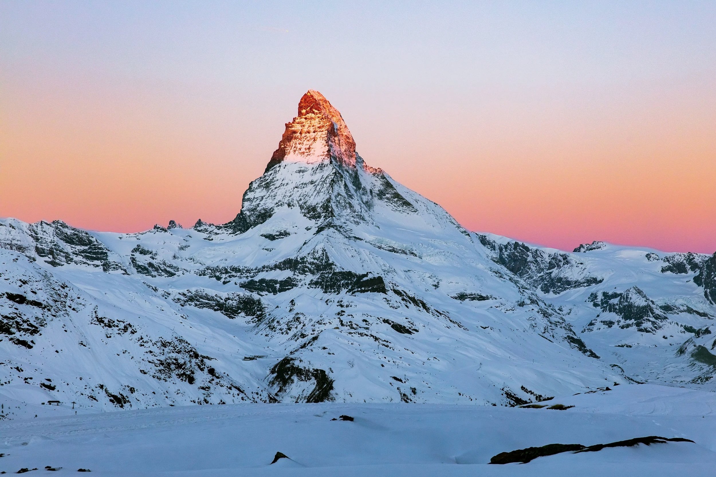 Snow-covered mountain peak at sunset with a pink and purple sky.