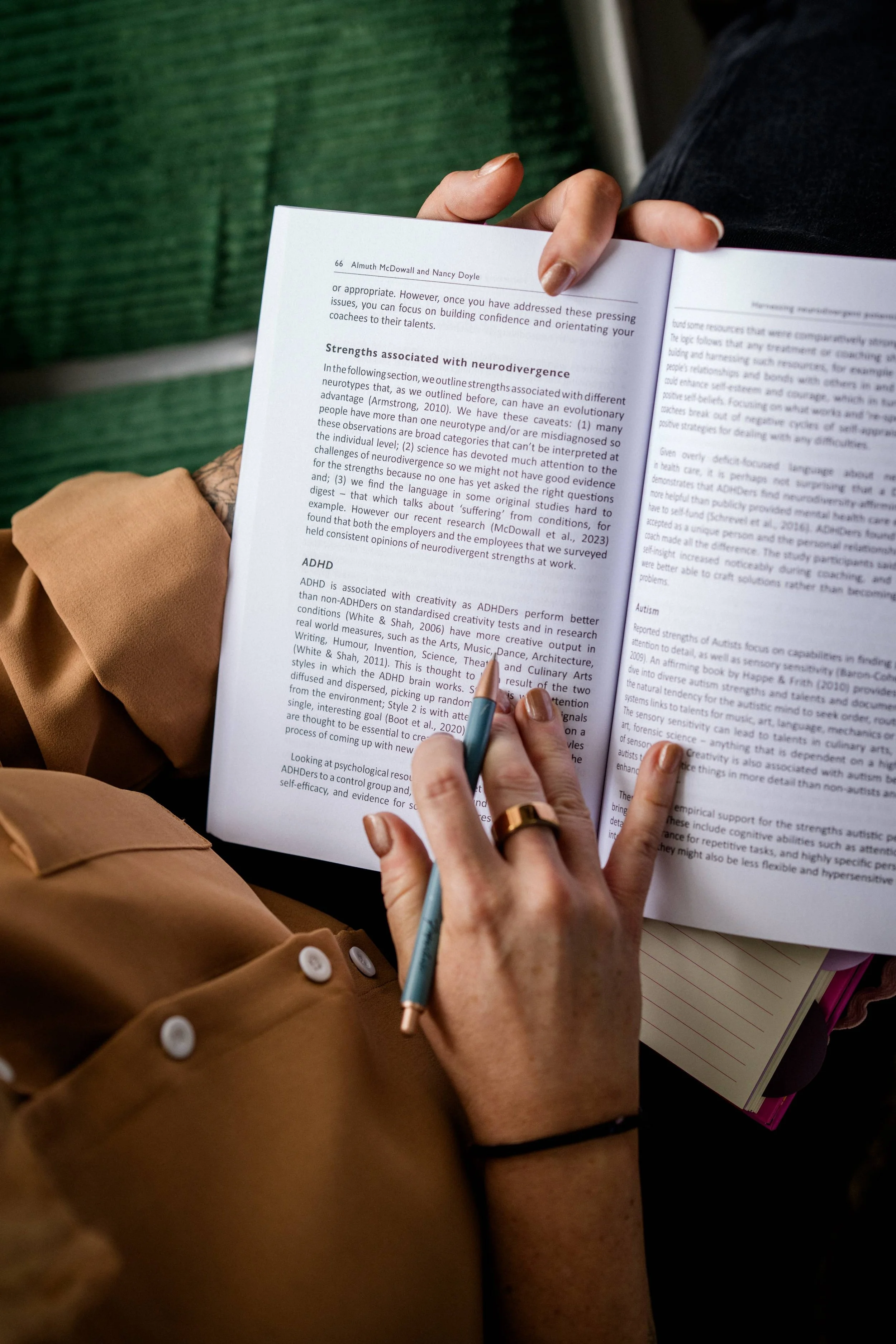 A person holding an open book and taking notes with a pen, with other notebooks nearby, seated on a green bench.