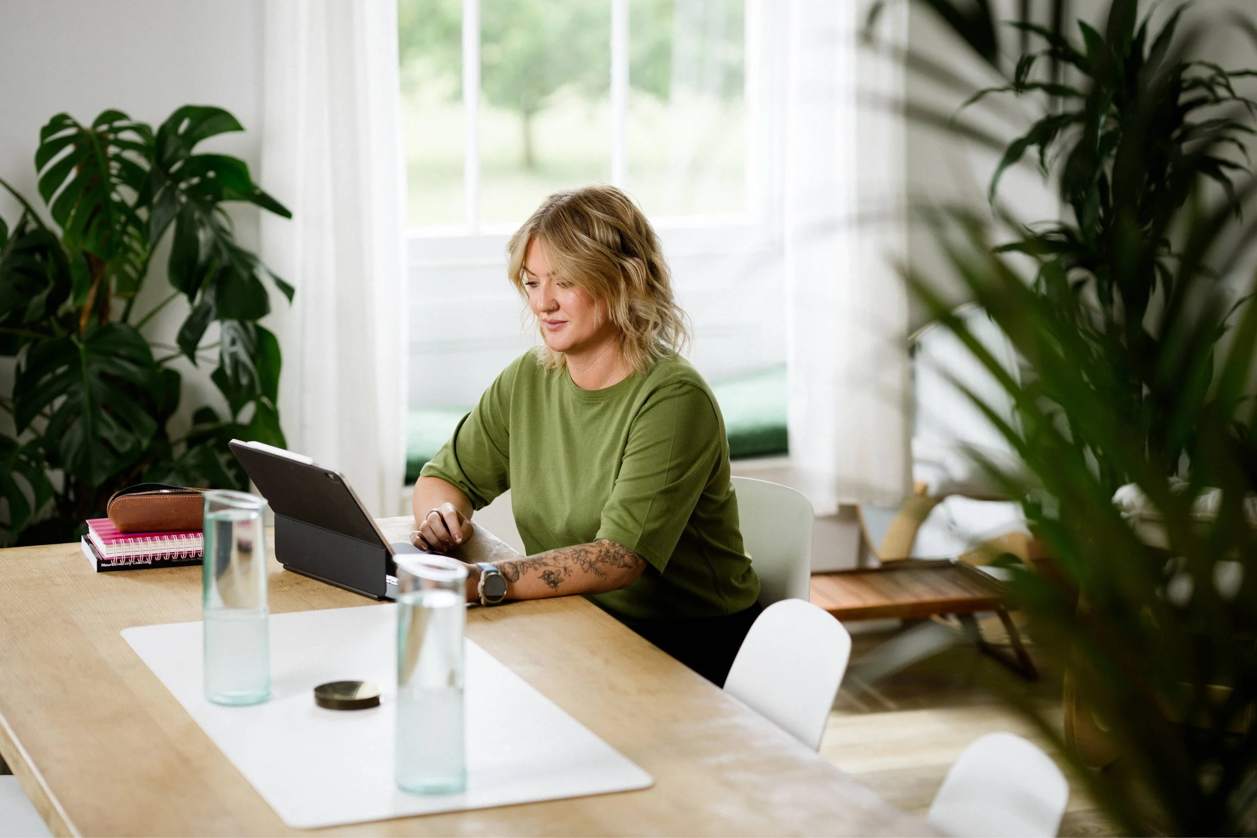 A woman standing in front of a whiteboard, smiling and holding a marker, leading a discussion with three women seated at a table in a conference room.