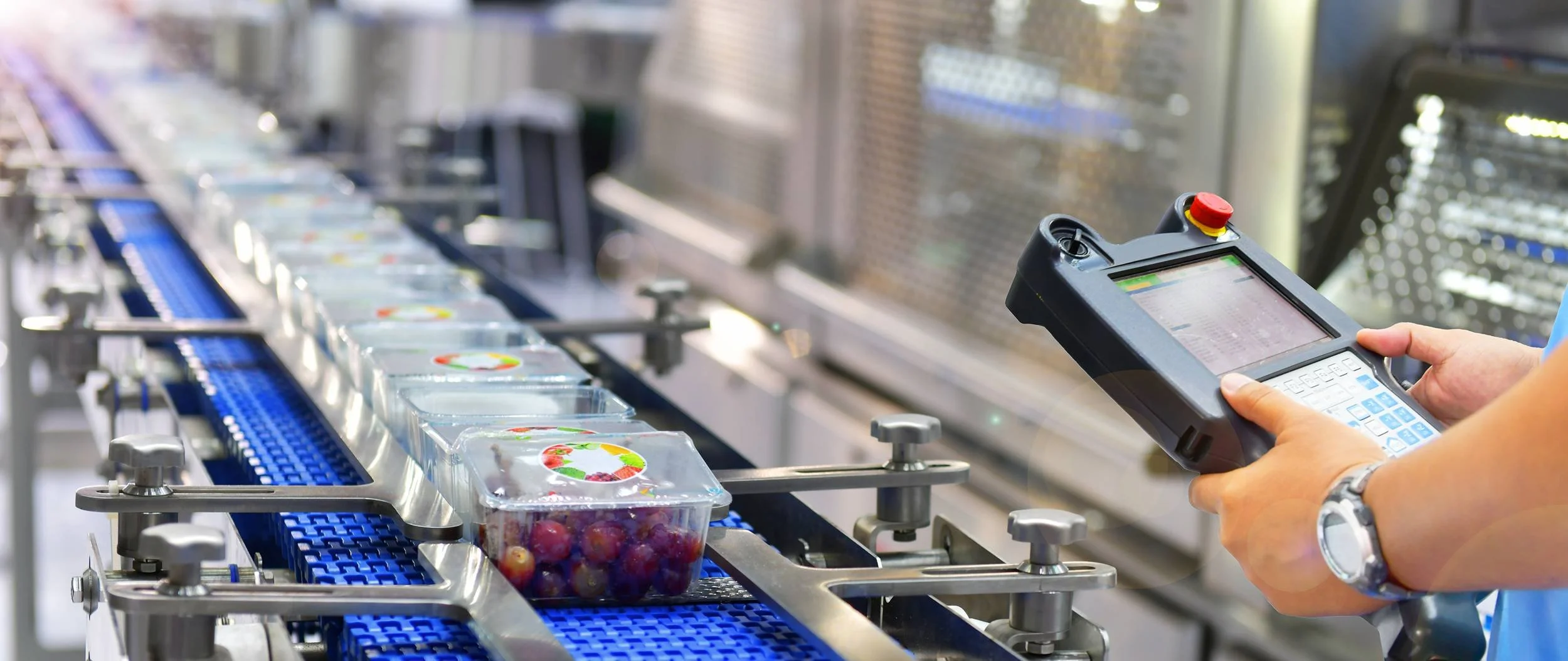 A conveyor belt with packaged food containers, with a person holding a handheld scanner or data terminal.