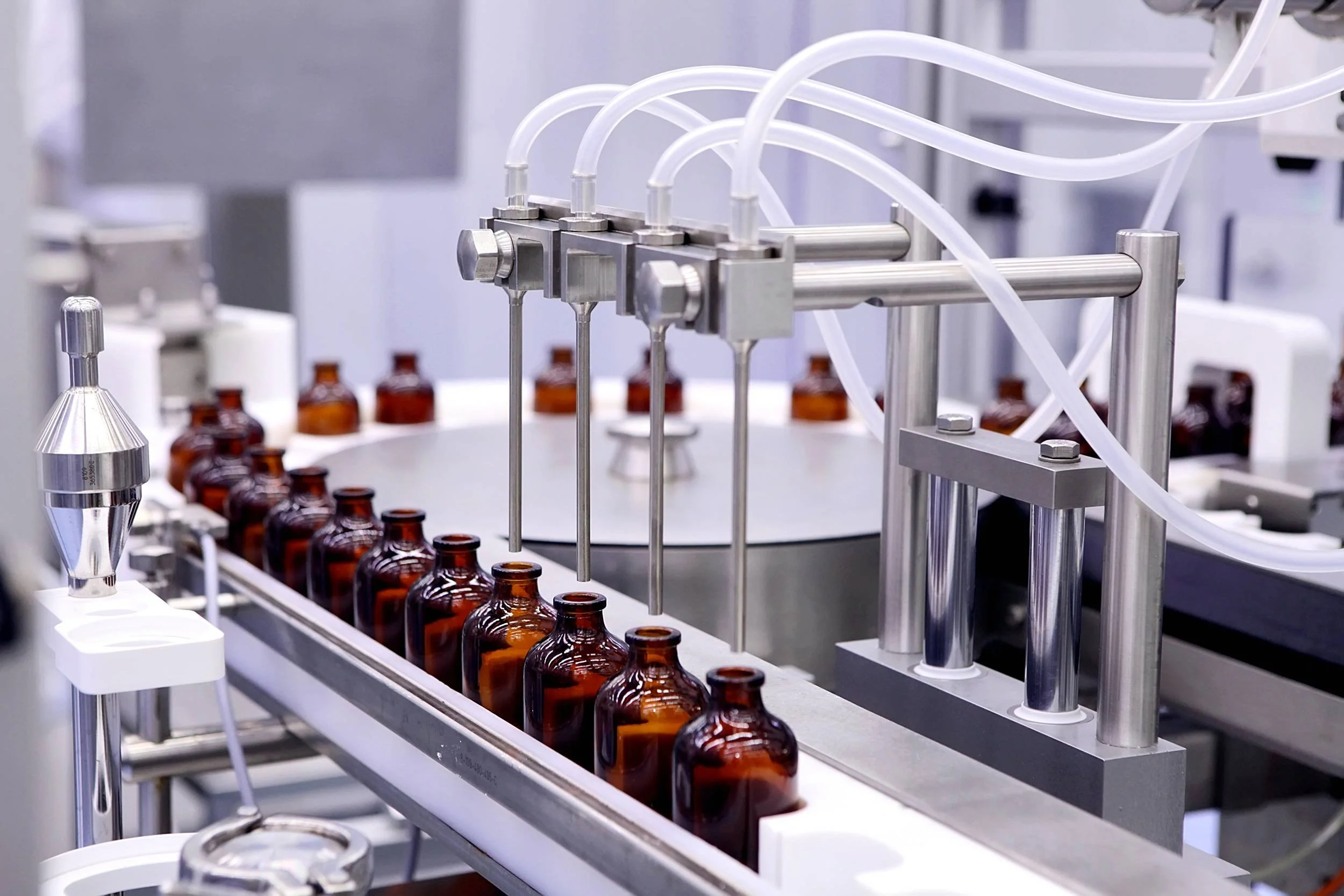Industrial machinery filling amber glass bottles with liquids in a laboratory or production facility.