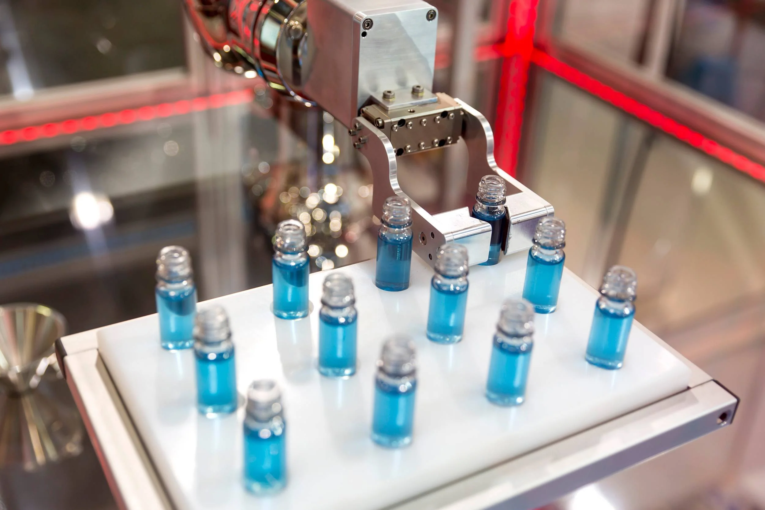 A machine filling small glass bottles with a blue liquid.