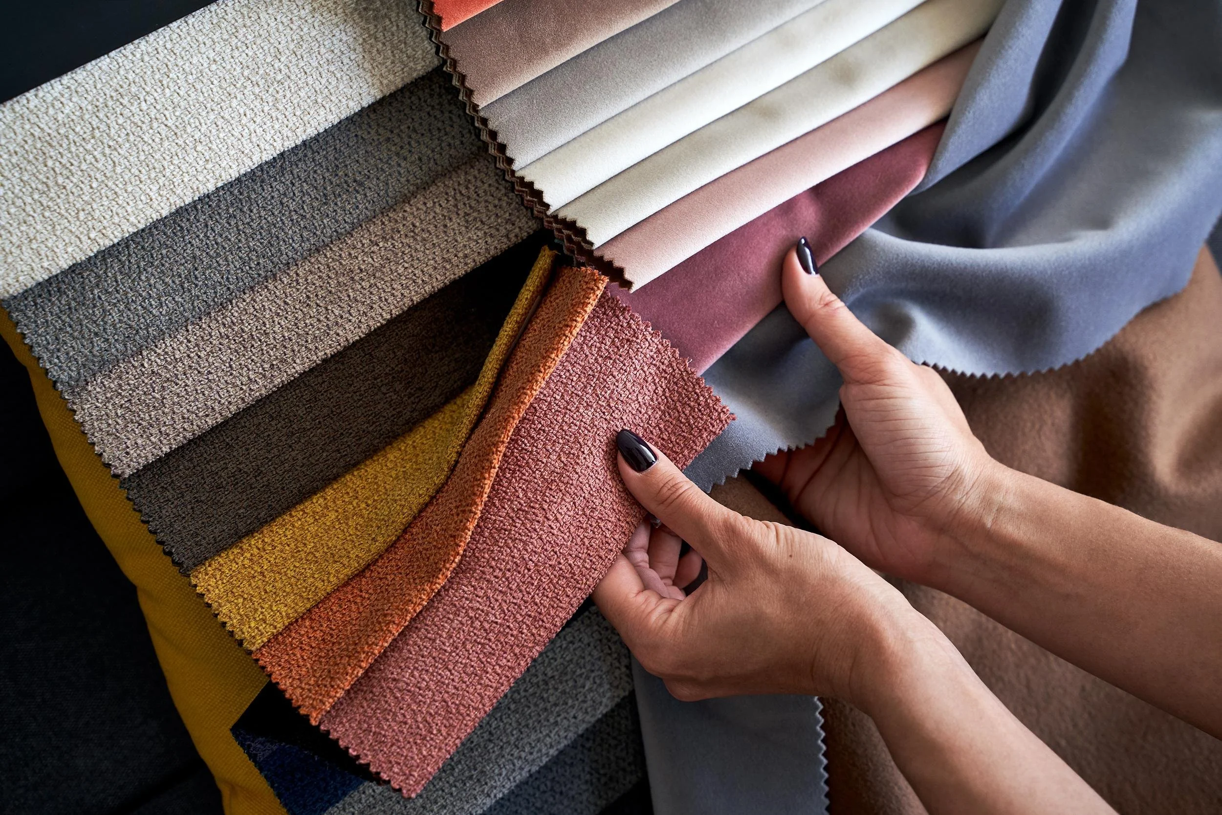 Person holding up fabric swatches in various colors and textures, including beige, pink, gray, and brown.