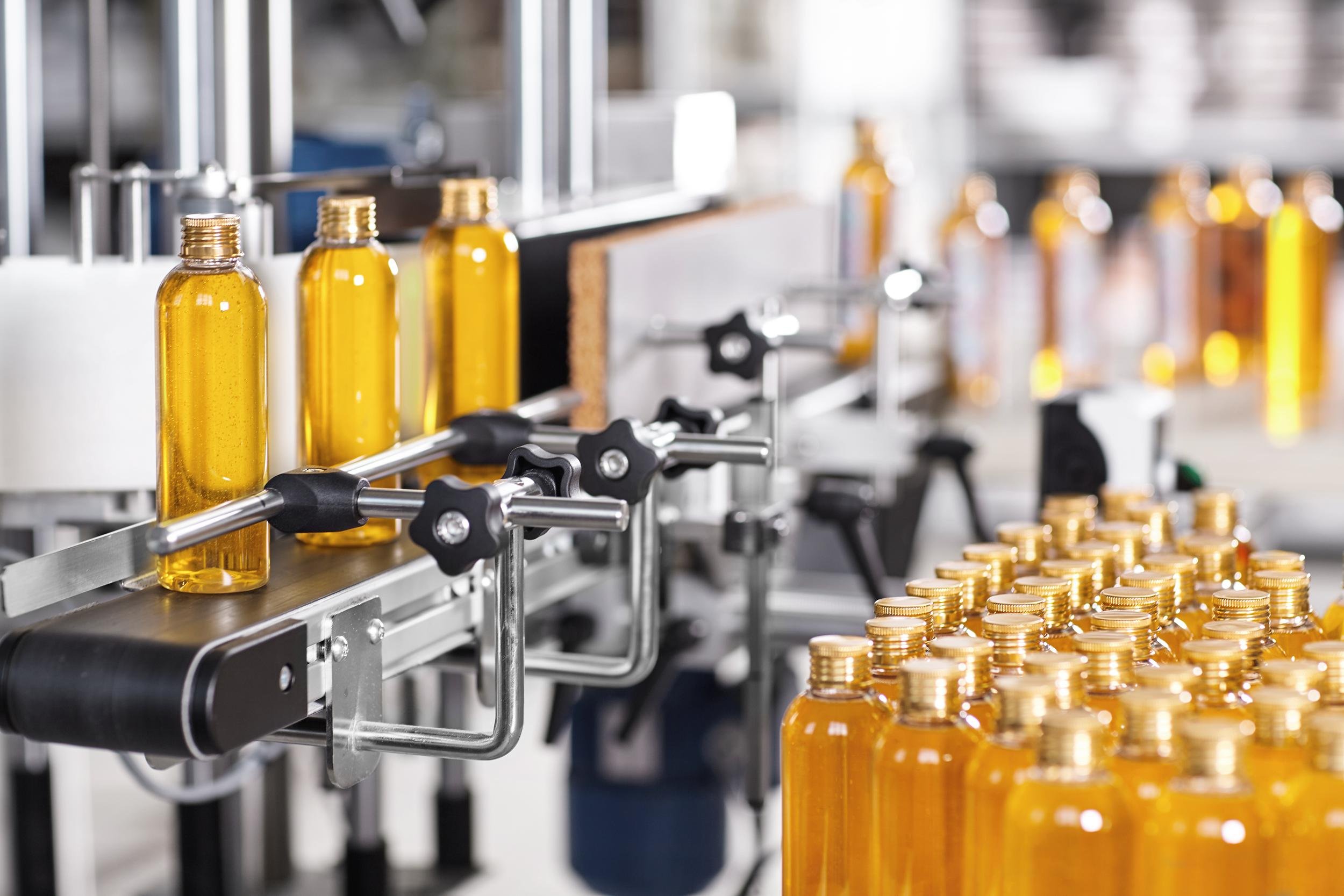 Bottles of yellow liquid on a production line with stacks of gold-colored capsules.