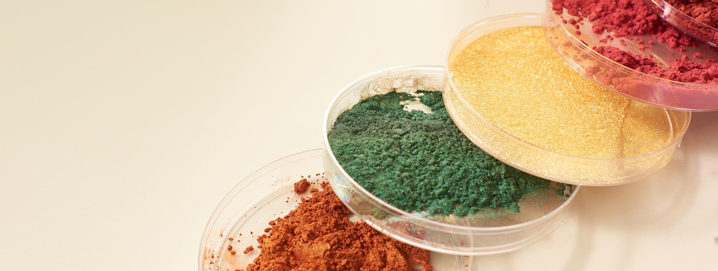 Containers of colorful powdered pigments including green, yellow, pink, and red.