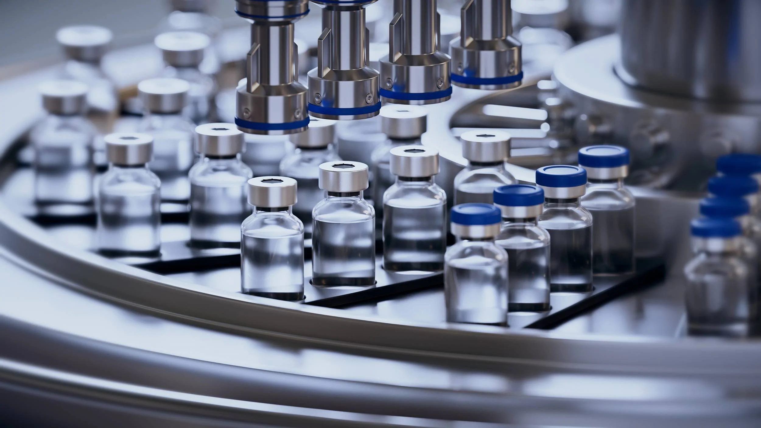 A close-up of a laboratory machine with small glass vials filled with a clear liquid, metal caps, and robotic arms or parts involved in an automated process.
