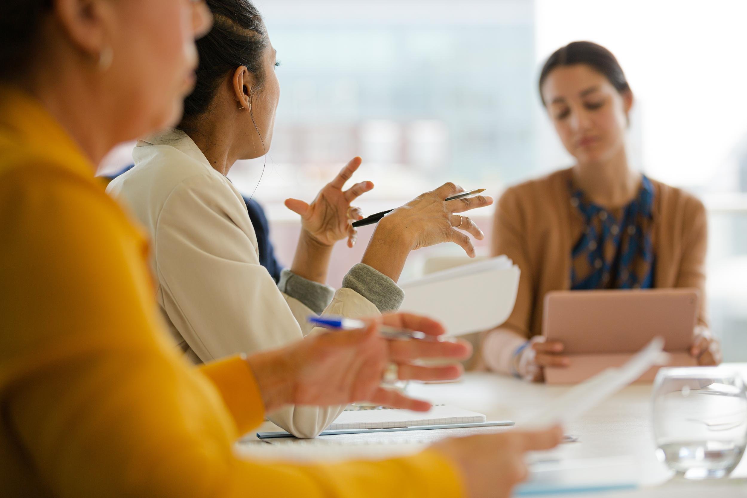 Group of diverse women engaged in a discussion in a professional setting, with some women taking notes and others listening attentively.