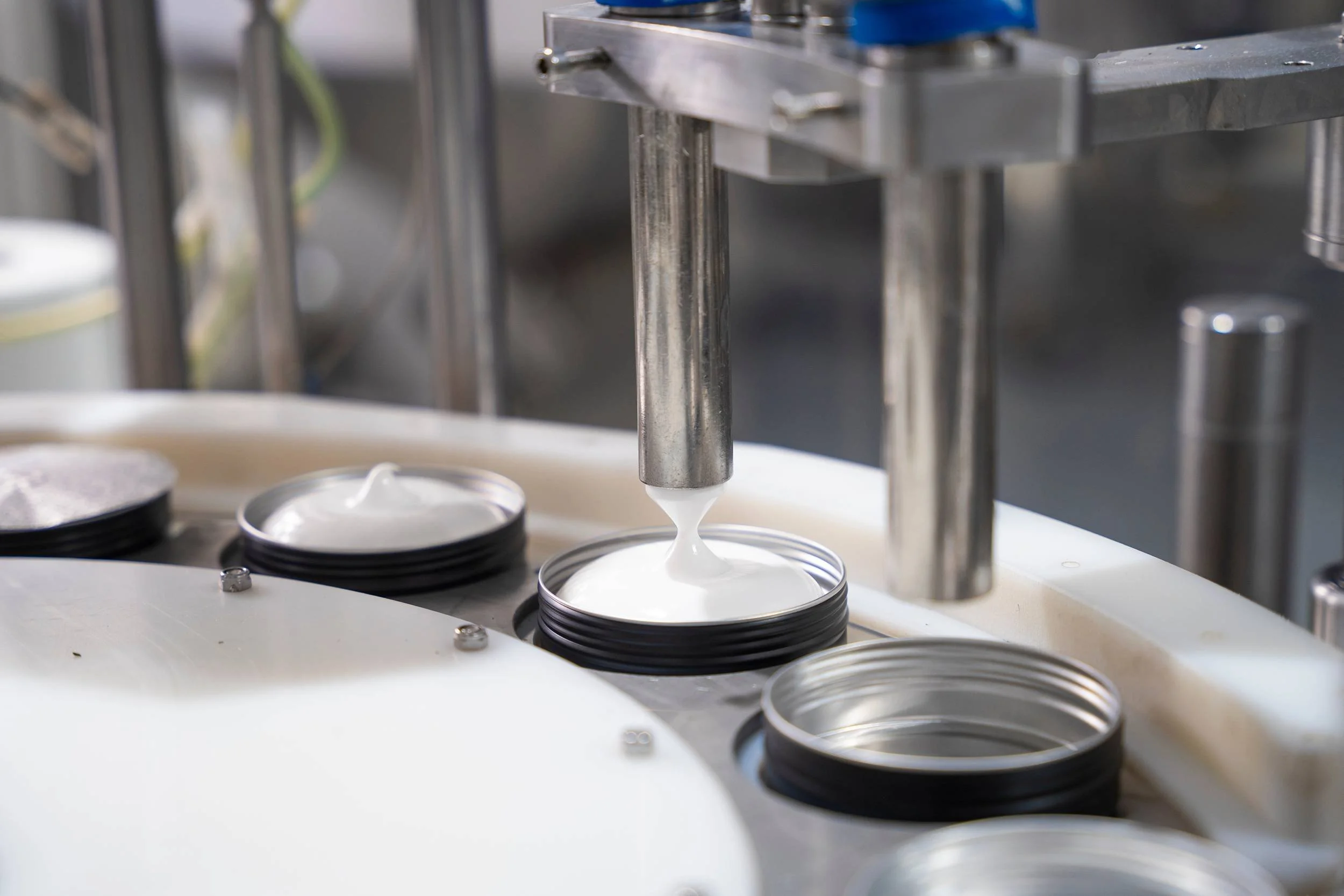 A machine dispensing white cream into open metal cans.