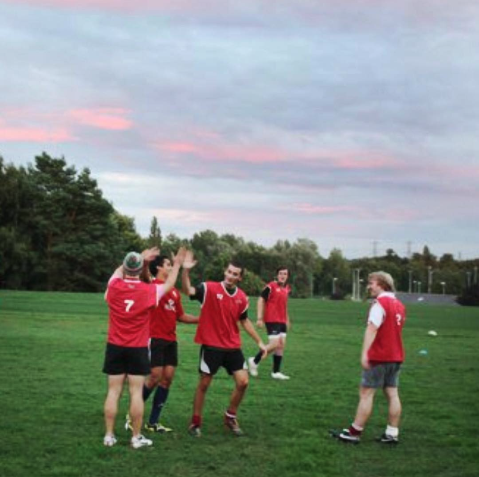 A group of men wearing red bibs celebrating on a training field as part of OGRFC first ever training