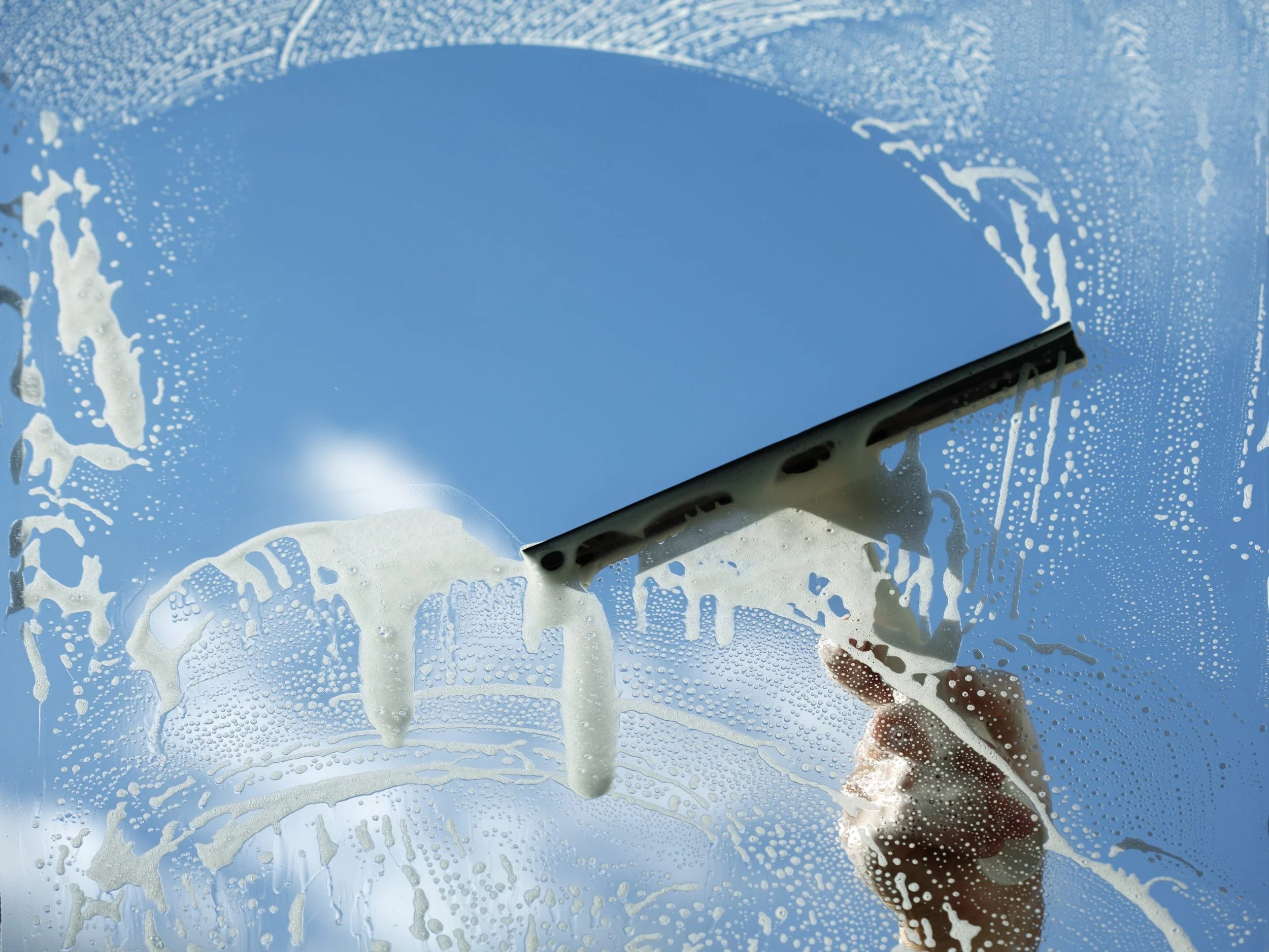 A person cleaning a glass window with a squeegee, with soap suds and water on the glass.
