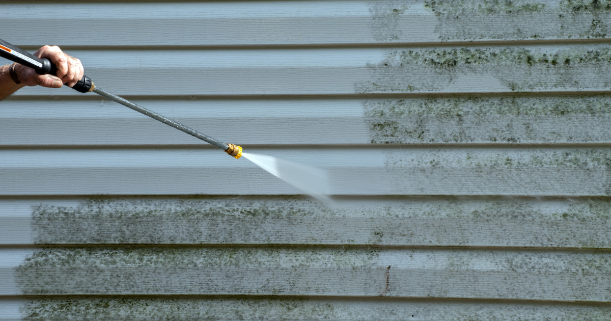 Person power washing the exterior siding of a house, removing dirt and mold.