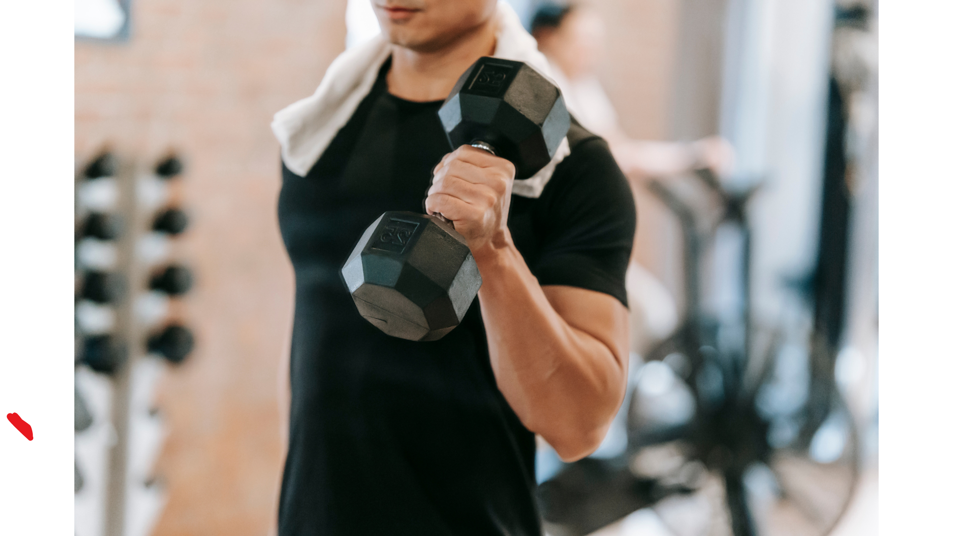A person lifting a black dumbbell in a gym with exercise equipment in the background.