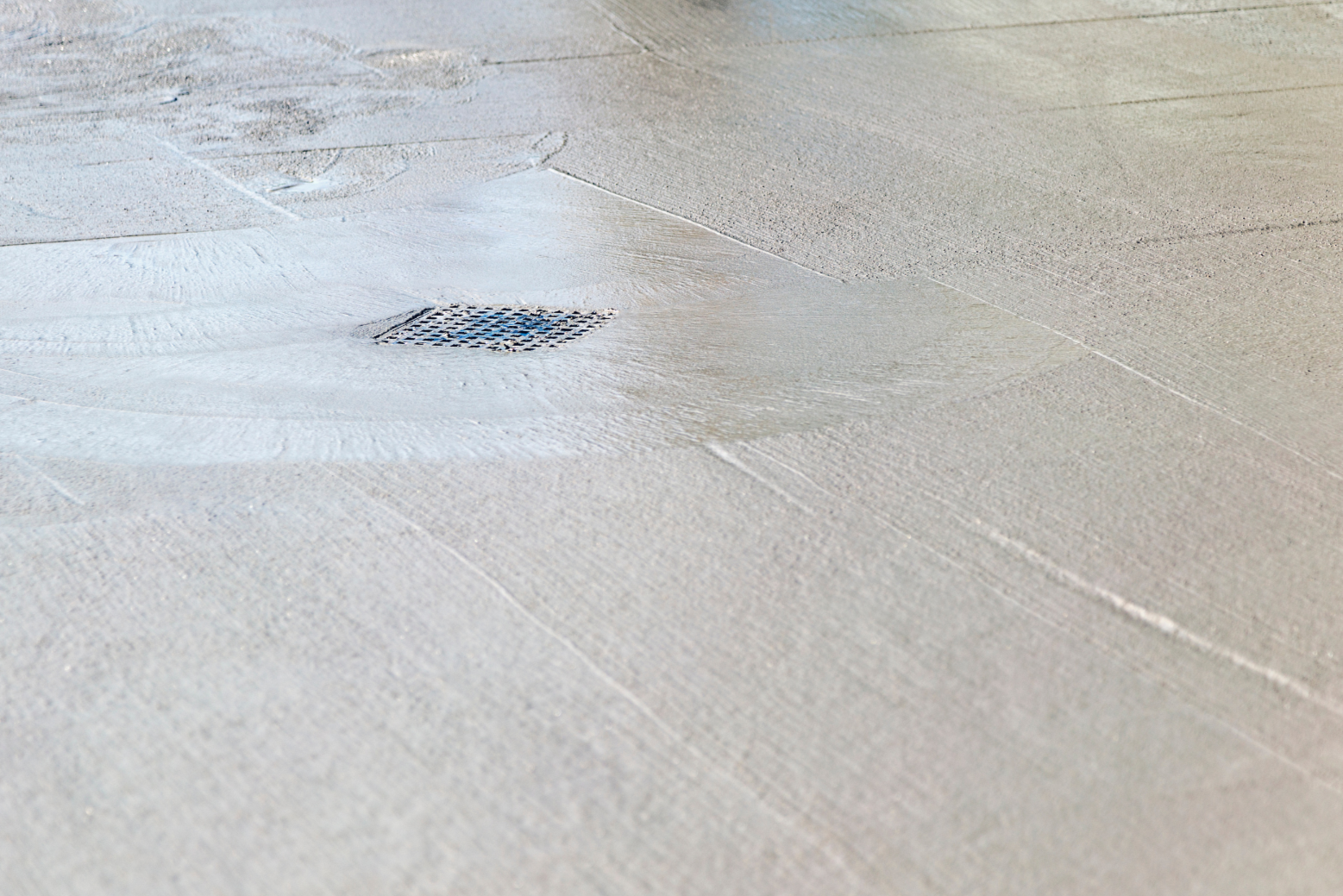 Close-up of a concrete sidewalk with a metal drainage grate in the center.