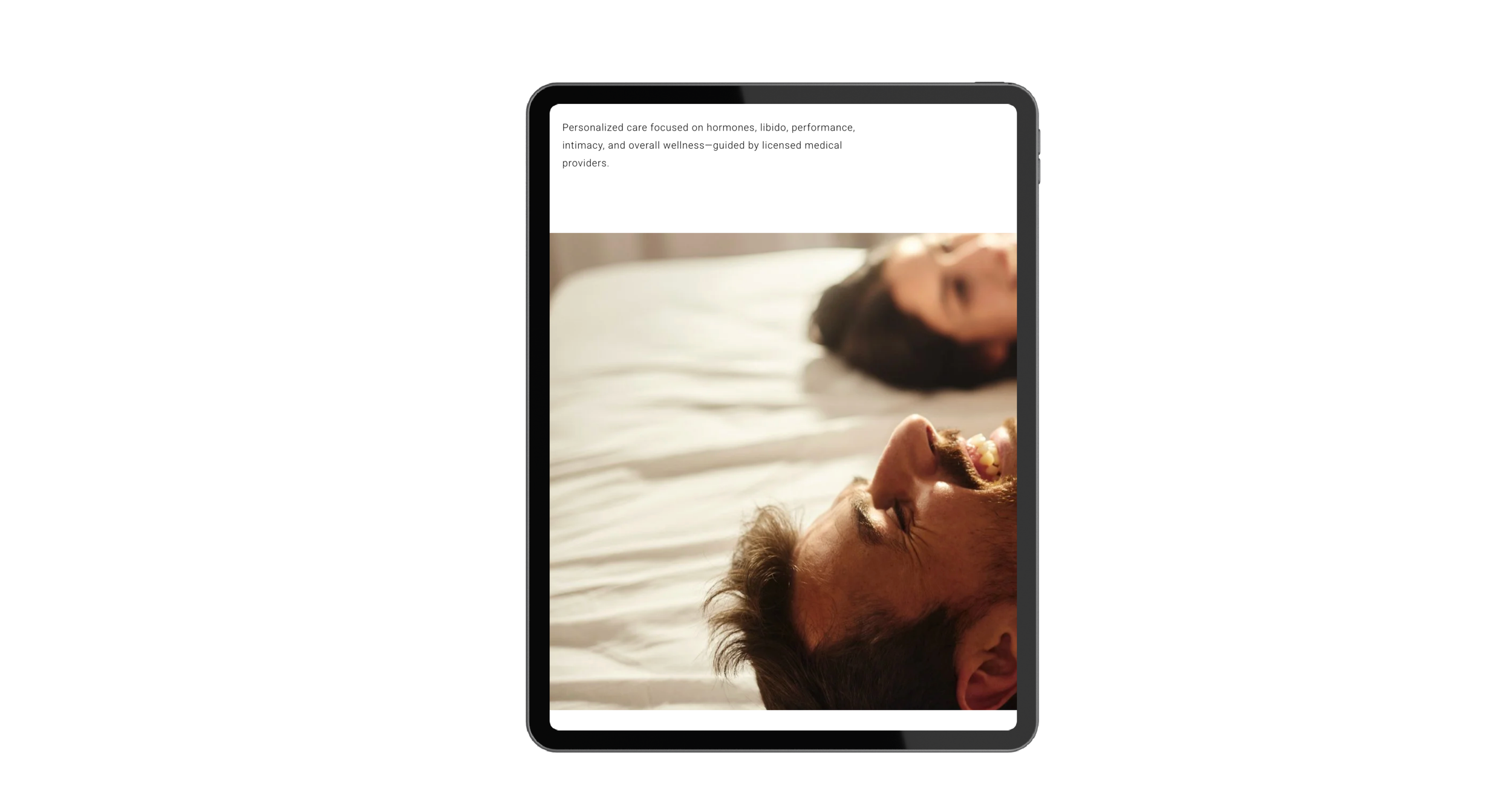 A smartphone displaying a messaging app with a photo of a smiling couple lying in bed, a woman in the background and a man in the foreground.