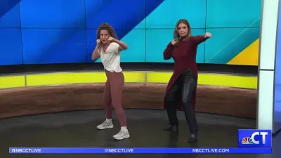 Two women dancing on a TV news set with a colorful background and NBC Connecticut branding.