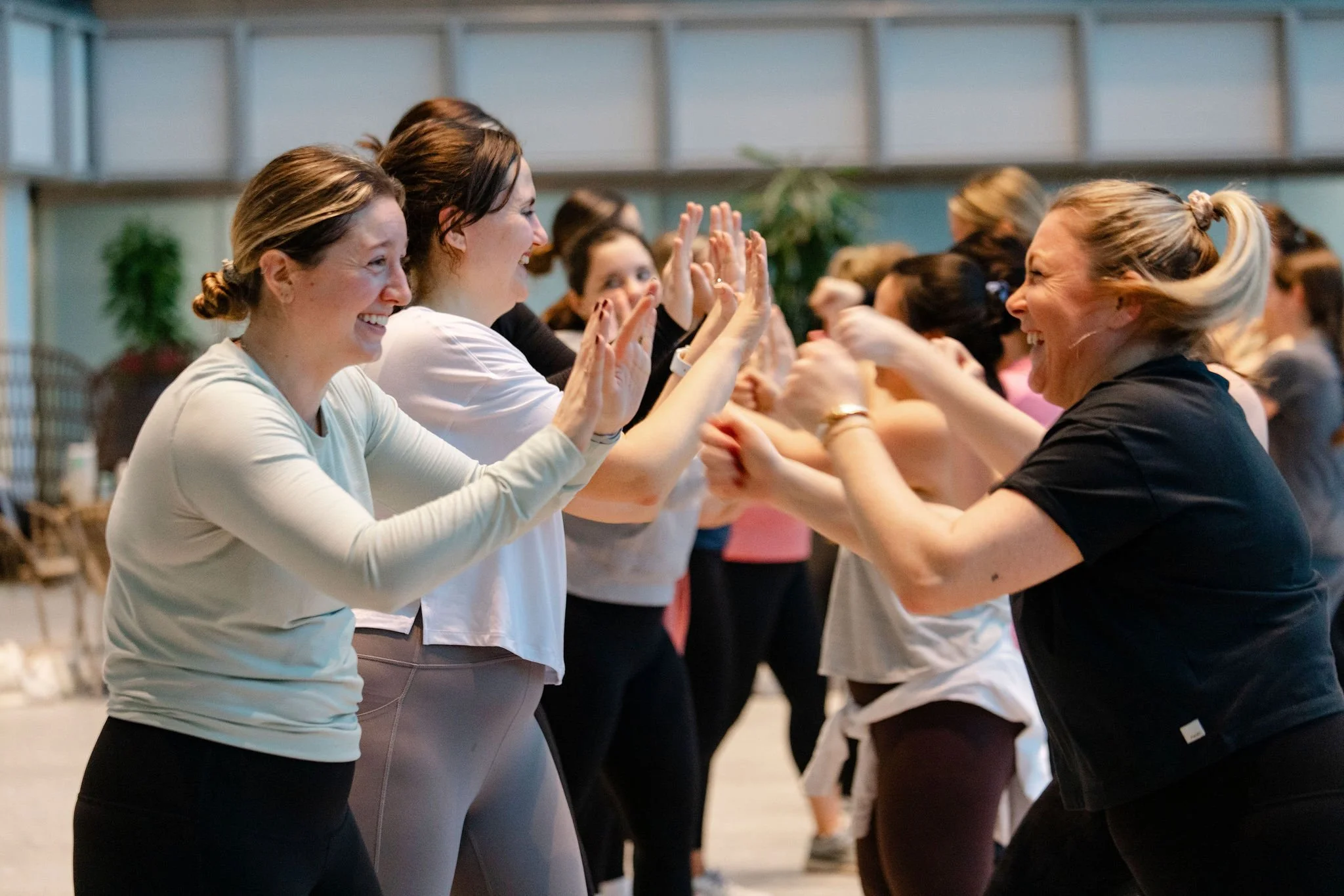 Women participating in a group activity, smiling, and high-fiving each other indoors.