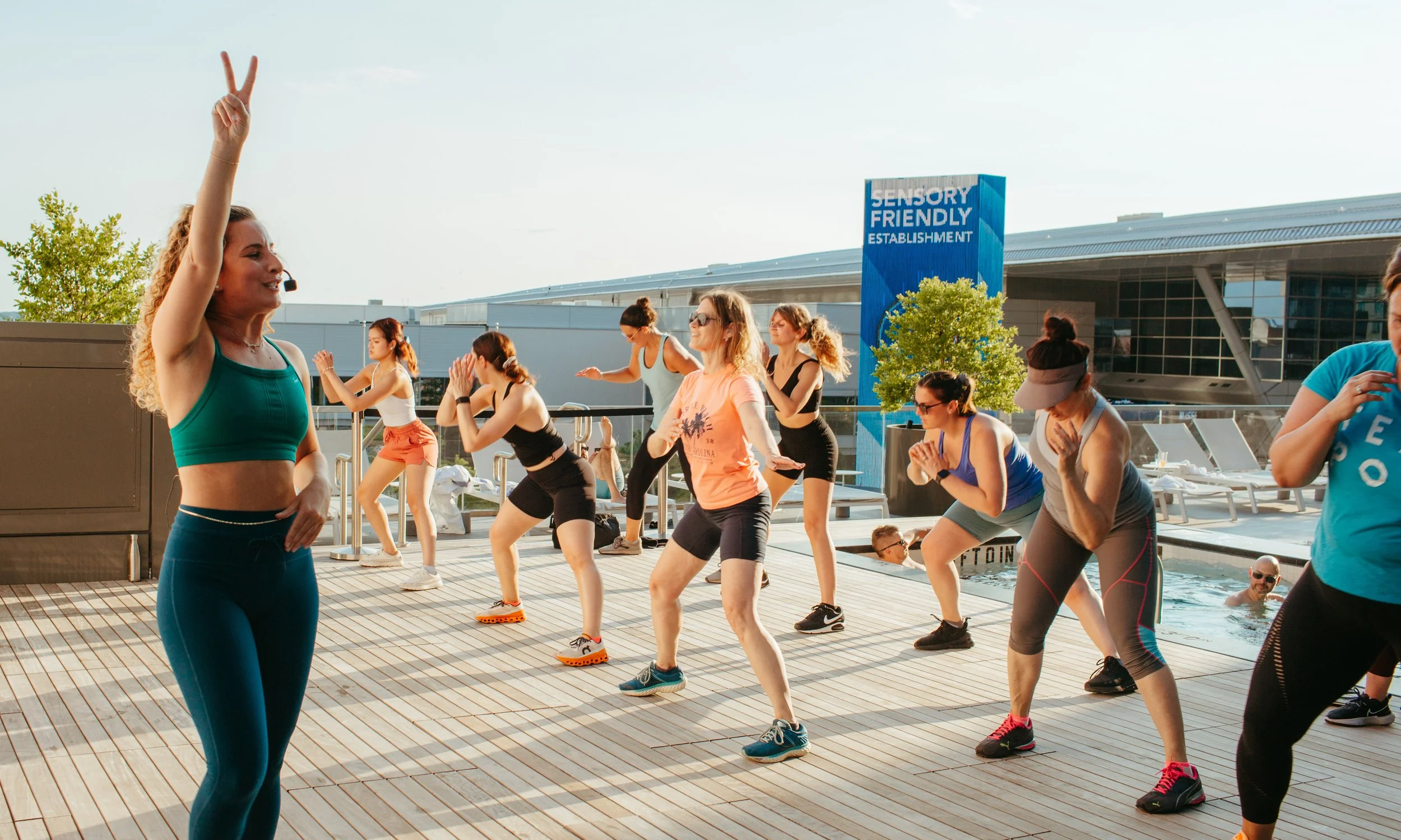 Group of women doing yoga or stretching exercises on a poolside deck during late afternoon sunlight