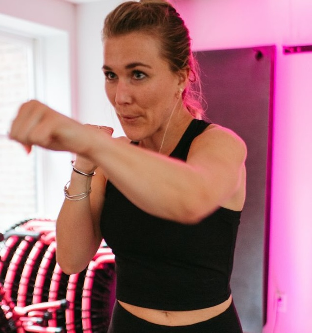 Woman punching in a fitness class with pink lighting.