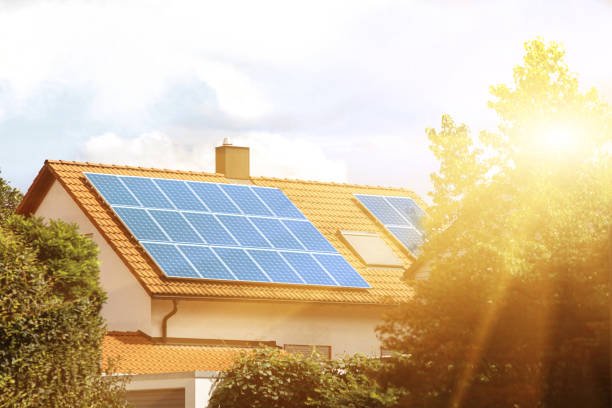 House with solar panels on the roof, surrounded by trees and sunlight.
