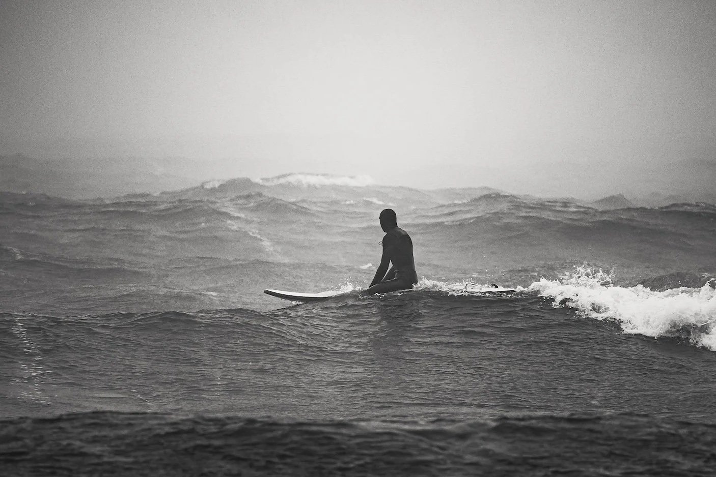 A person sitting on a surfboard in the ocean, surrounded by waves. Lake Superior, Duluth, MN