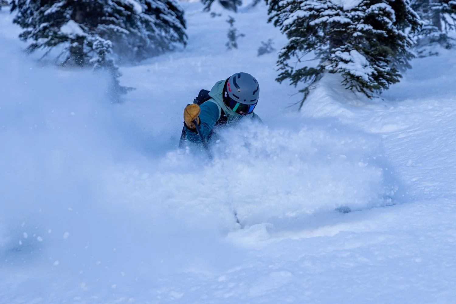 A skier wearing a helmet and goggles skiing through deep snow in a winter forest.