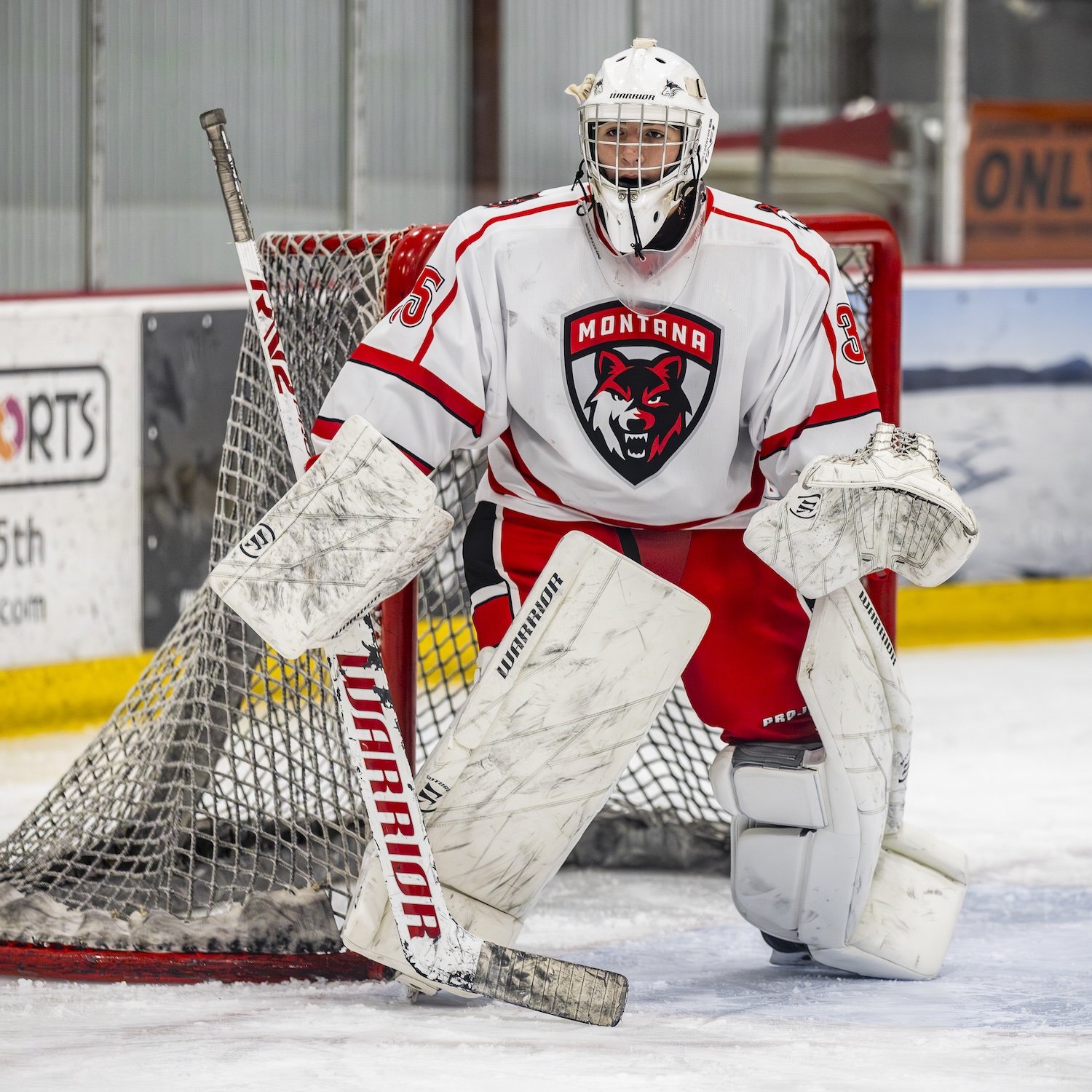 Ice hockey goalie in white and red uniform standing in front of the net.