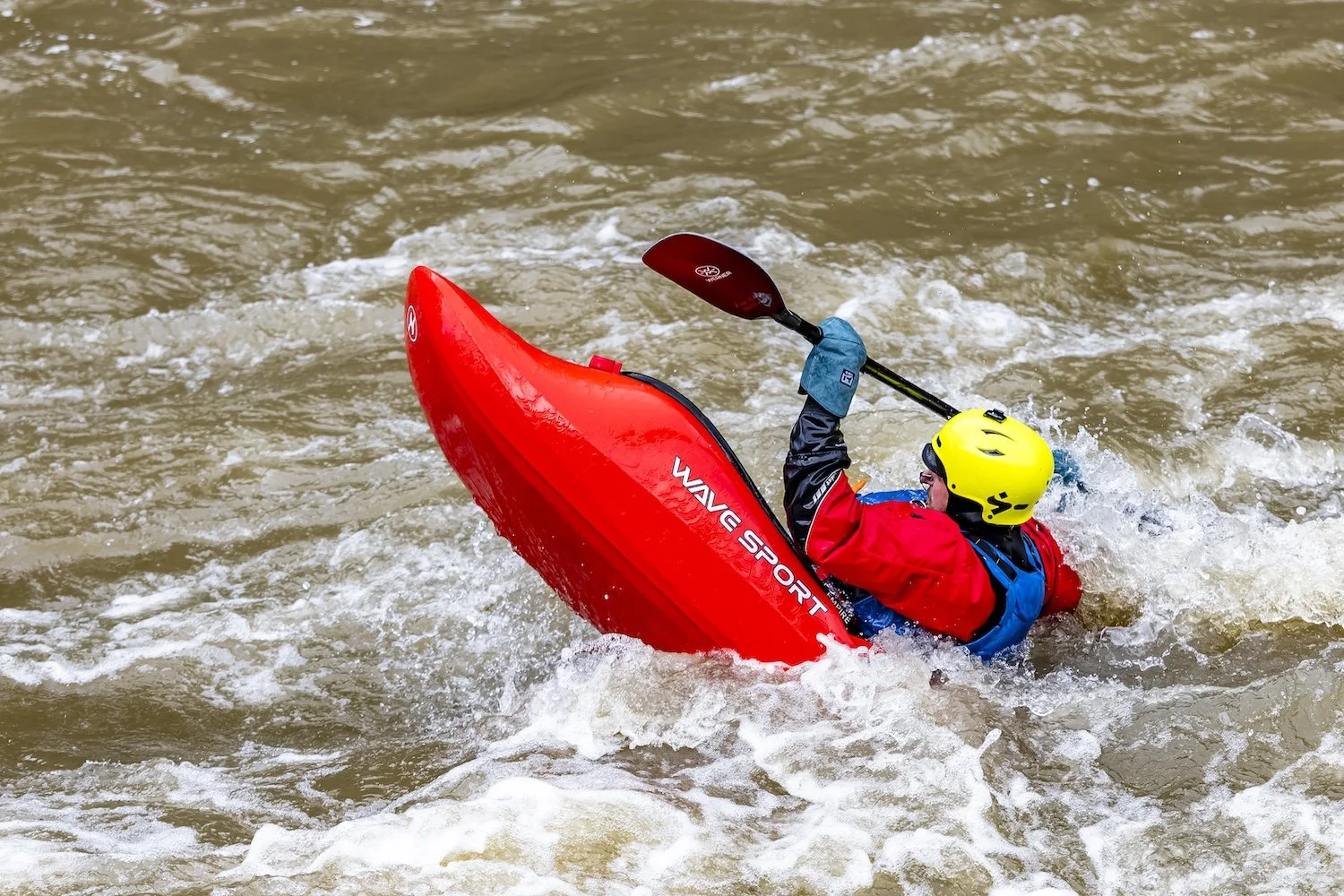 Person wearing a yellow helmet and a red drysuit kayaking in rough water on a river. Gallatin River, Montana, USA.