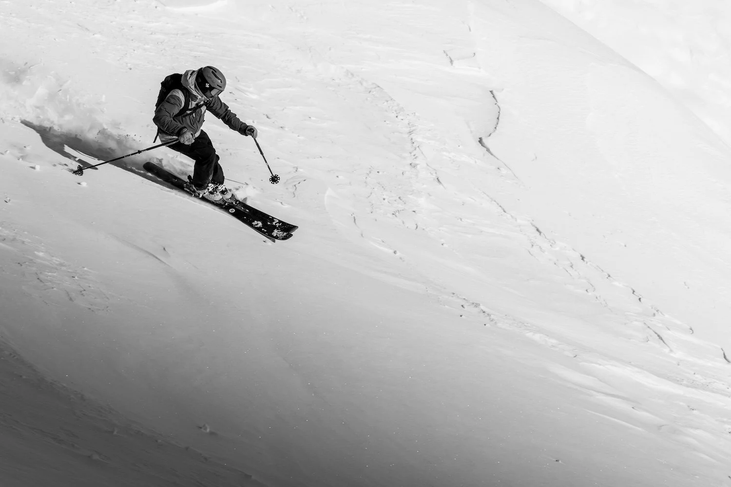 A person skiing down a snowy mountain in black and white, wearing a helmet and winter gear.