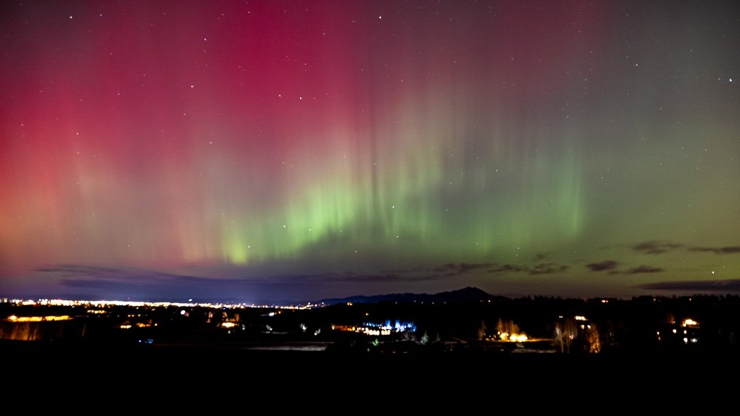 Northern Lights (aurora borealis) in the night sky above a rural landscape with city lights. Bozeman, Montana, USA