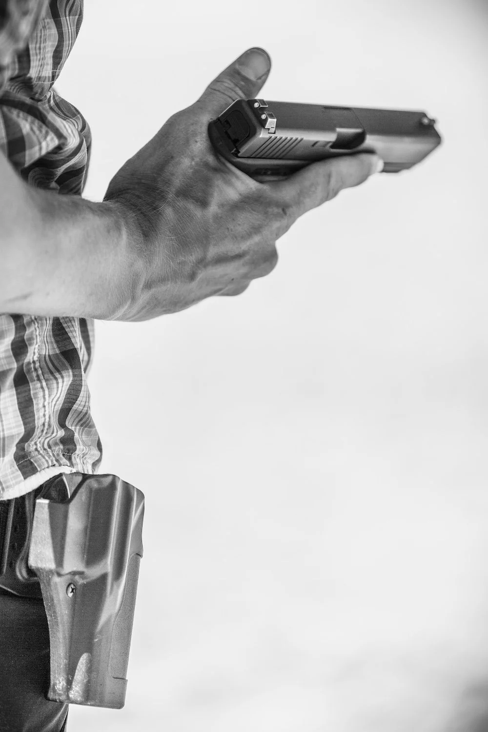 Close-up of a person holding a handgun, wearing a plaid shirt, with a holster on their belt. Montana, USA