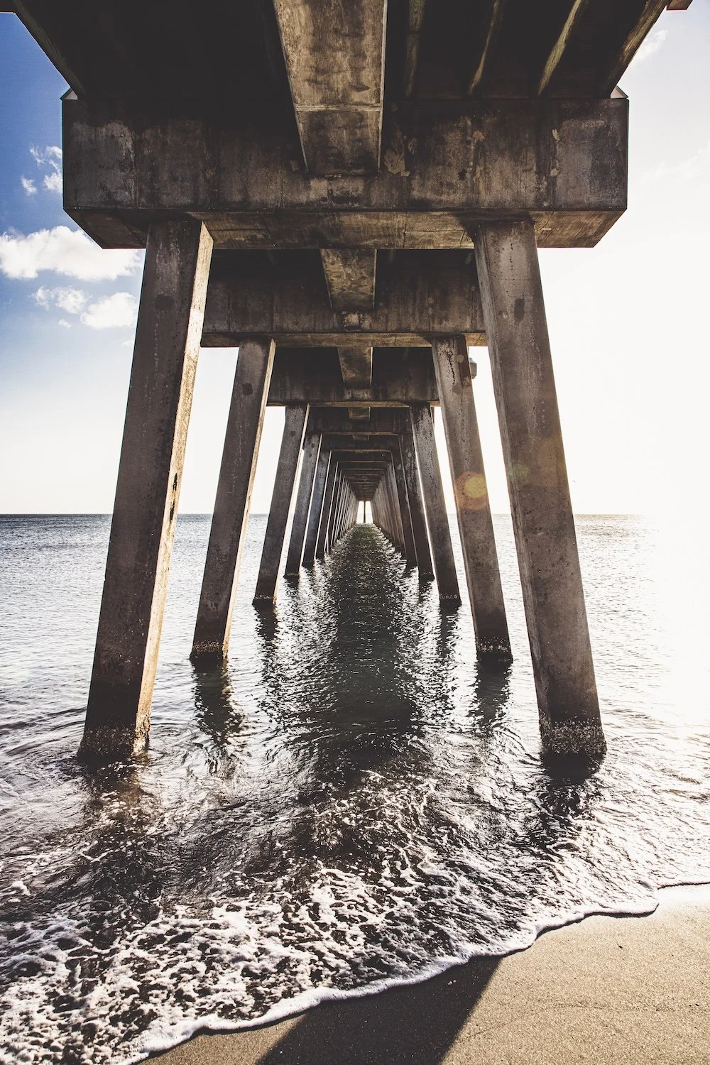 Beach level view of pier extending into the ocean, with water and sandy beach visible. Venice Beach, Florida.