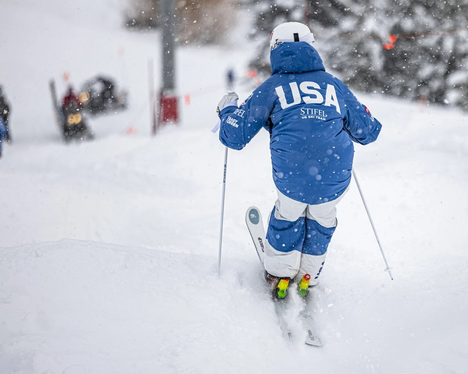 A skier in blue and white gear with 'USA' on the back skis through snowy terrain during a winter sports event.