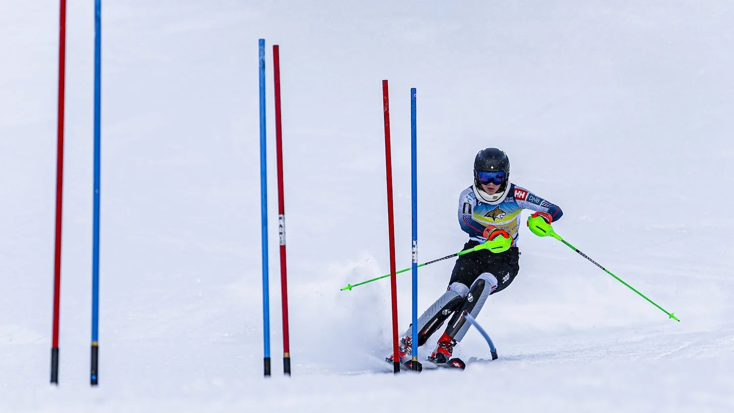 A young skier navigating through a slalom race course on snow, wearing a helmet, goggles, and colorful racing gear.