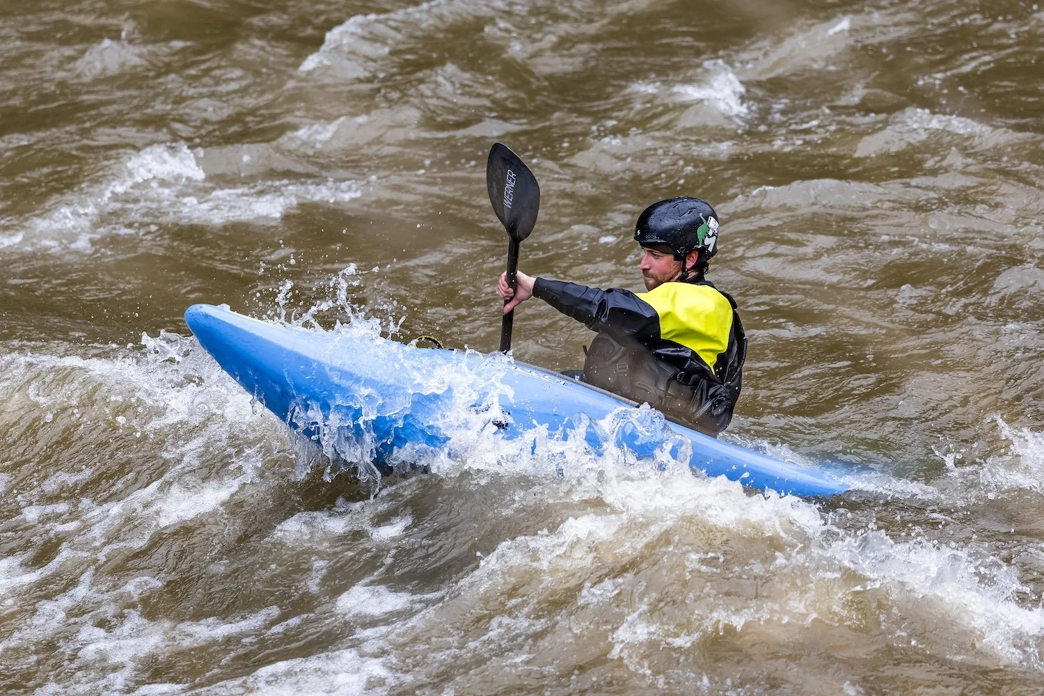 Man kayaking on choppy water, wearing a black helmet and a yellow life jacket. Gallatin River, Montana, USA