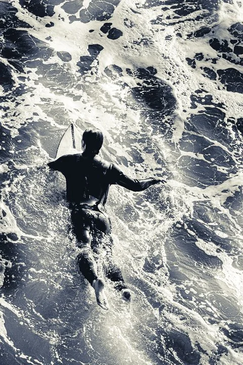 A surfer paddling on the Pacific Ocean, viewed from behind. Manhattan Beach, California, USA.