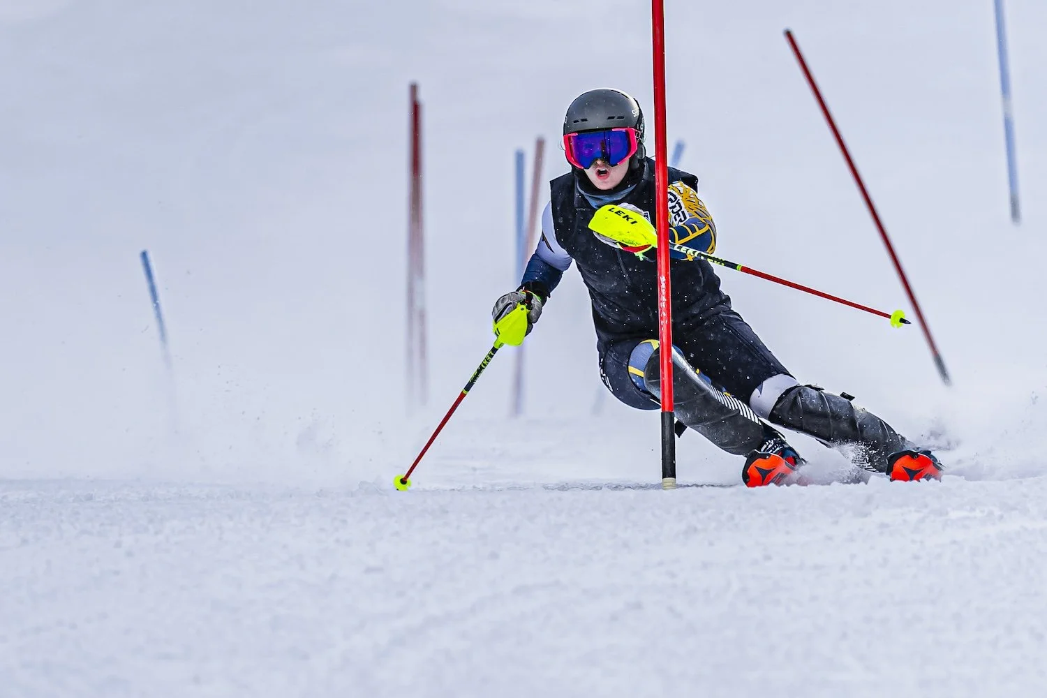 A young skier in a helmet and goggles navigates a slalom course on snowy terrain, maneuvering around red and blue gates.