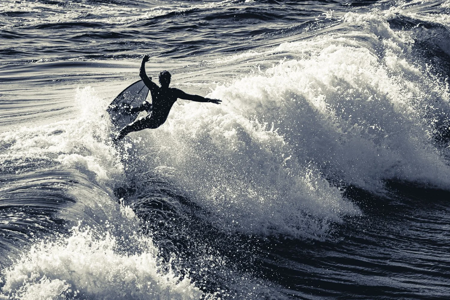 Silhouette of a surfer riding a wave in the Pacific Ocean during daytime. Manhattan Beach, California, USA.