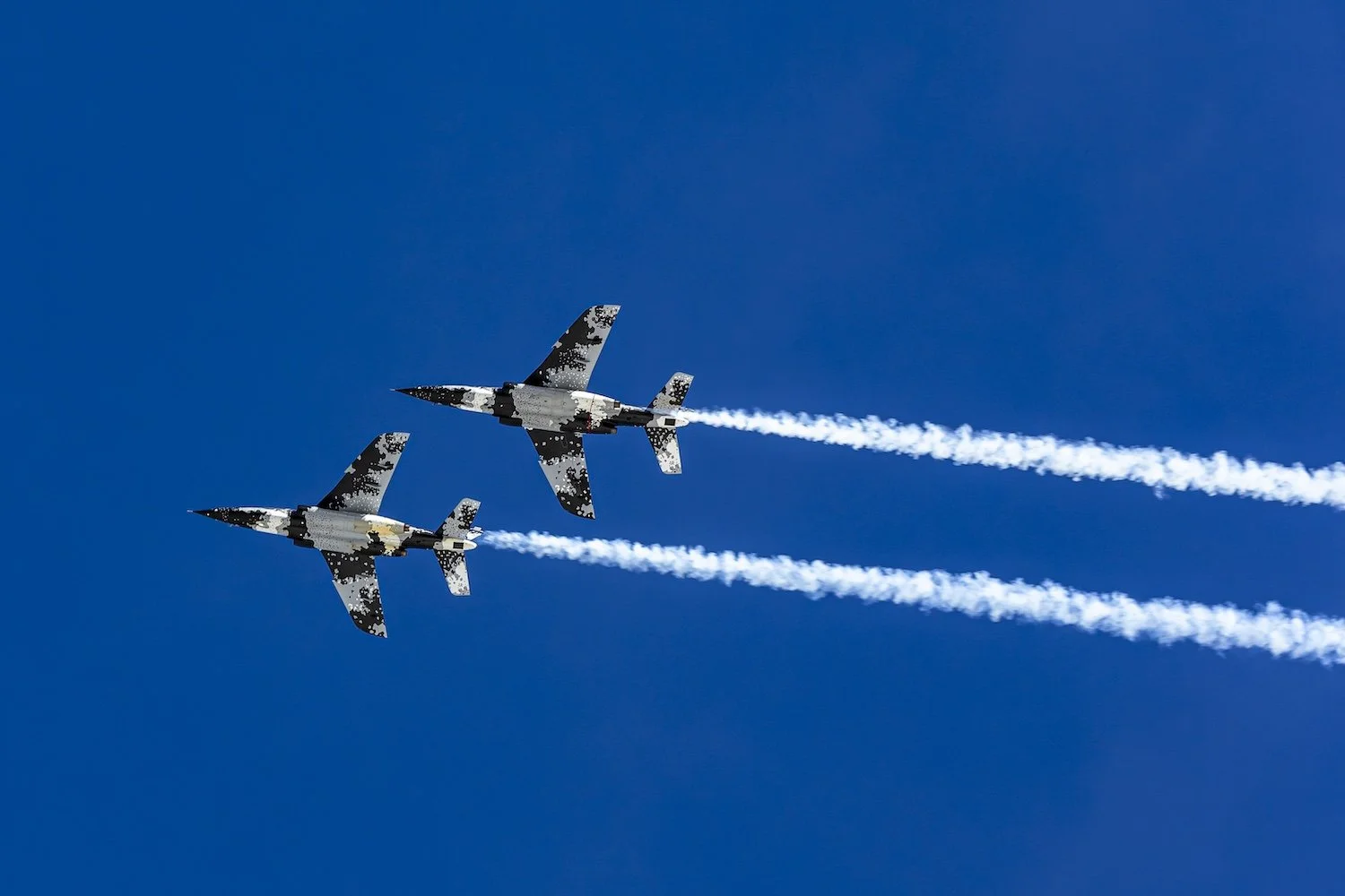 Two fighter jets flying in formation against a clear blue sky, leaving white smoke trails behind them. F.A.T. ICE RACE 2026, Big Sky, Montana USA. Dan Lakatos Photo
