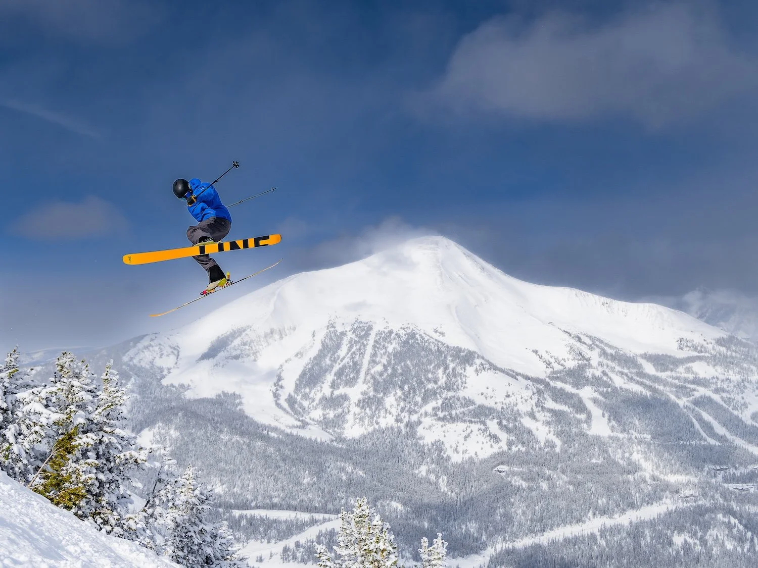 A skier in blue jacket and black helmet jumping off a snowy mountain peak in winter.