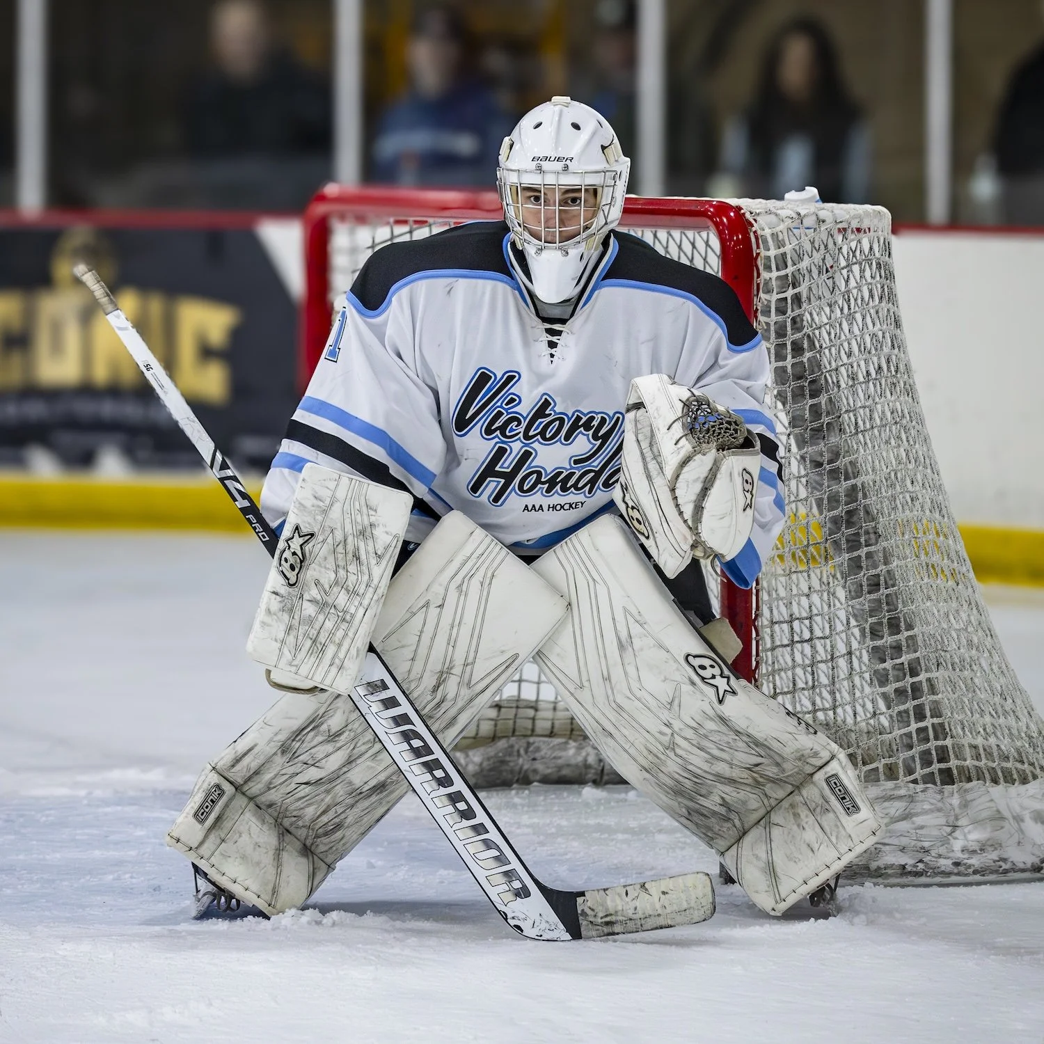 Ice hockey goalie wearing a white jersey with blue accents and 