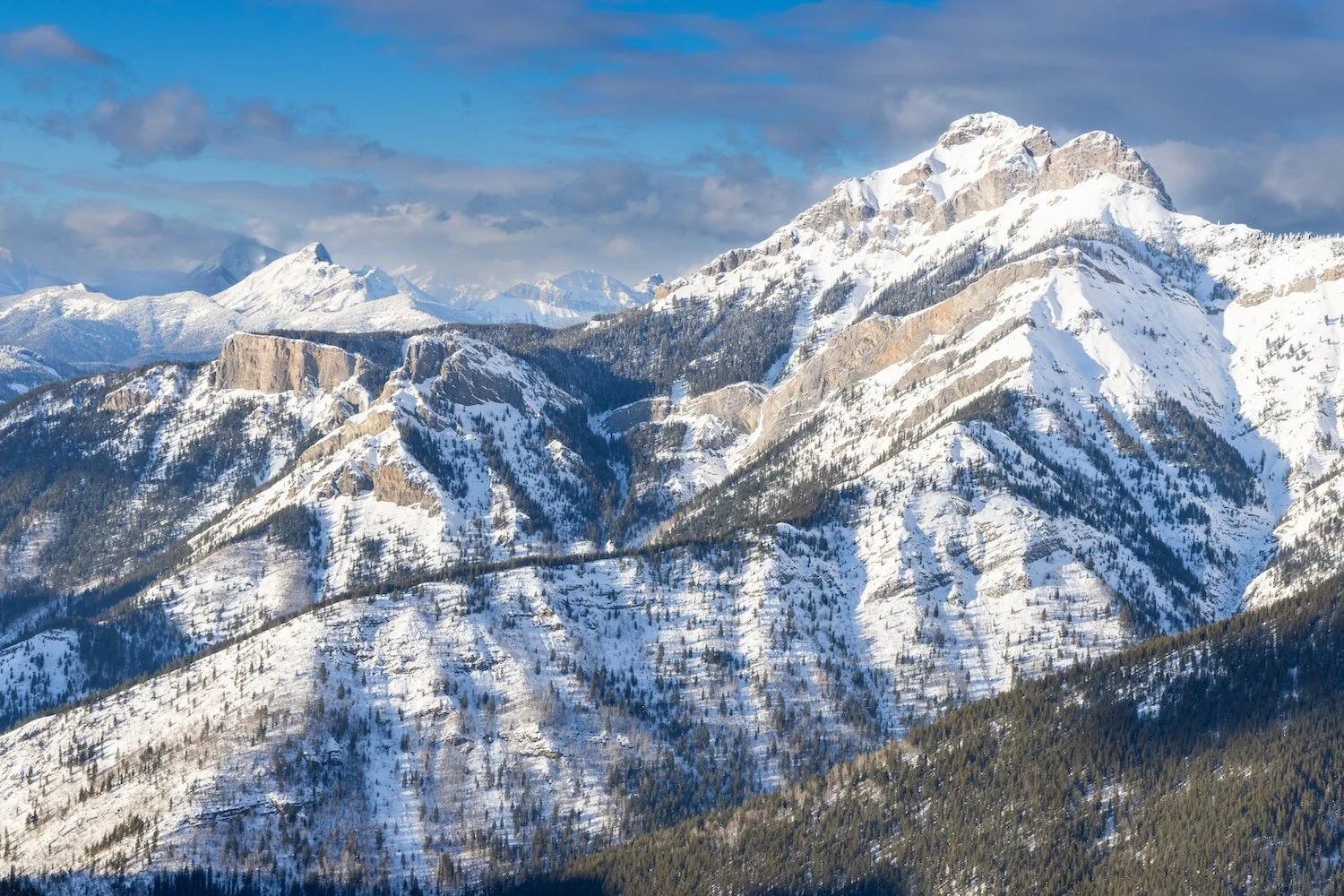 Snow-covered mountain range under a partly cloudy sky. Island Lake Lodge. Fernie, British Columbia, Canada