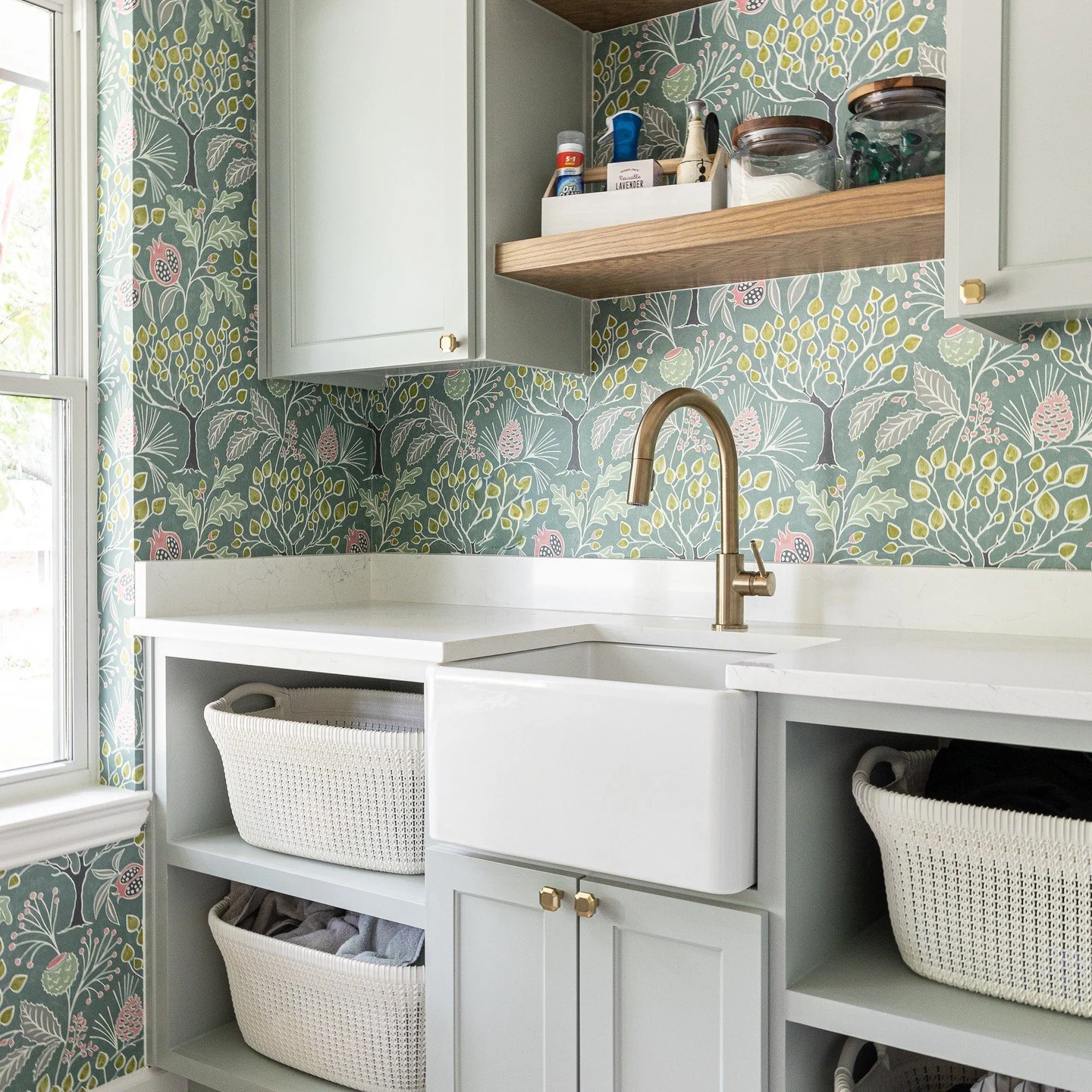 Kitchen with white cabinetry, a farmhouse sink with bronze faucet, open shelves with jars, and floral wallpaper in shades of green, pink, and yellow.