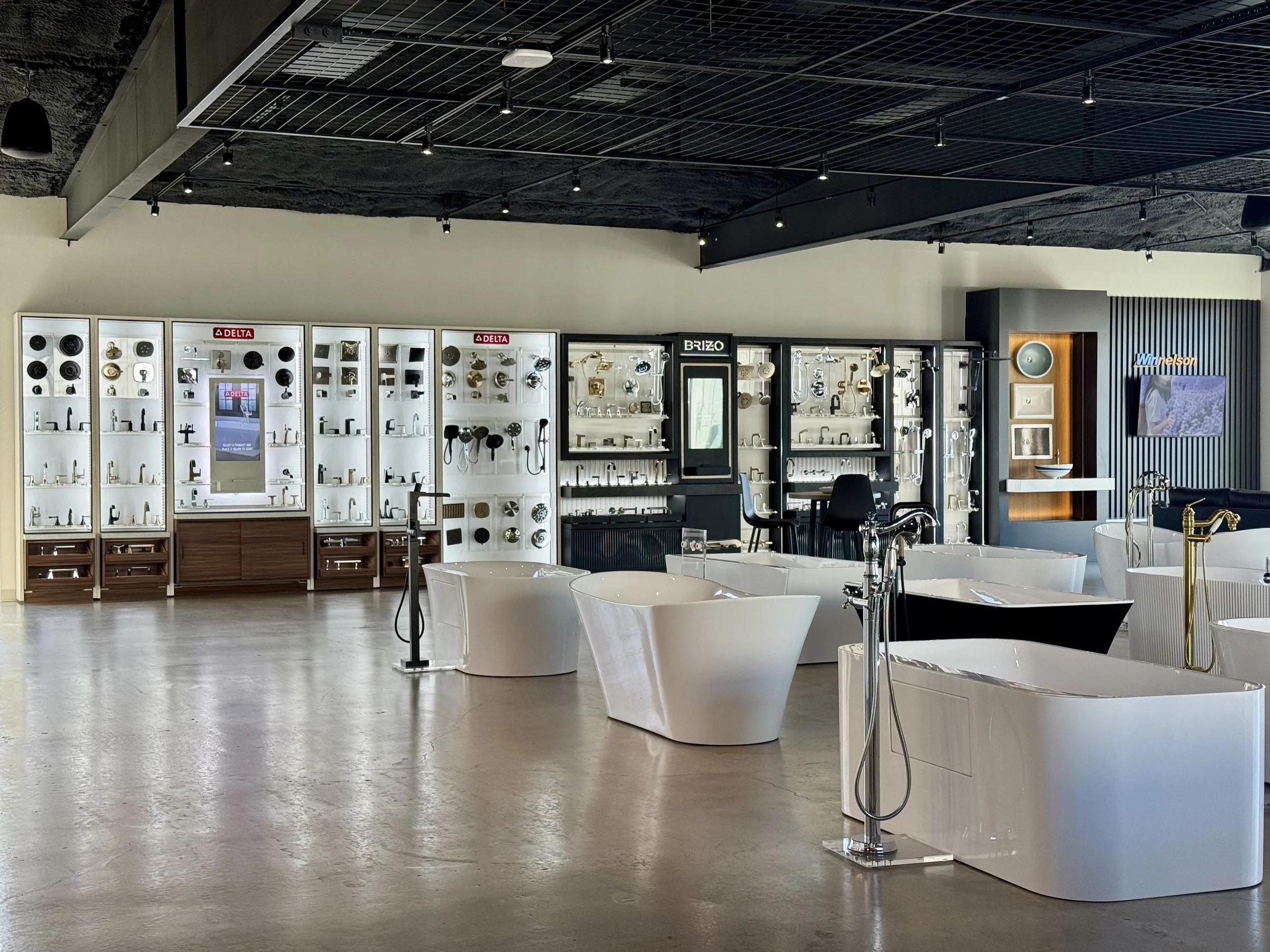 Interior view of a bathroom fixture showroom displaying faucets, sinks, and plumbing fixtures on display cabinets with bright lighting and a modern design.