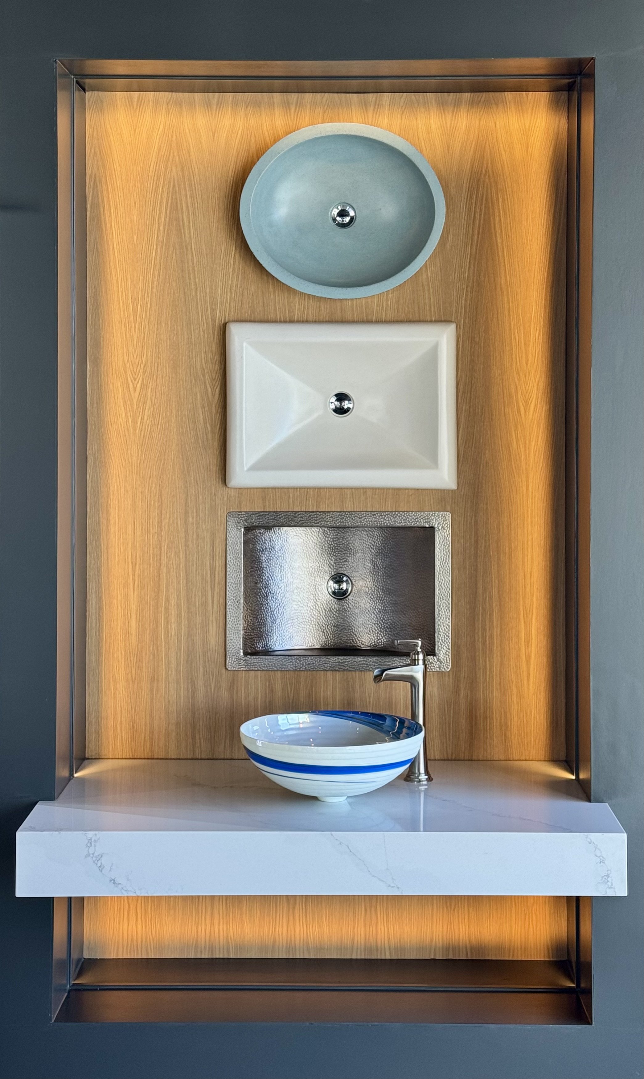 An art display featuring various sink designs on a wooden background with a marble surface in the foreground.