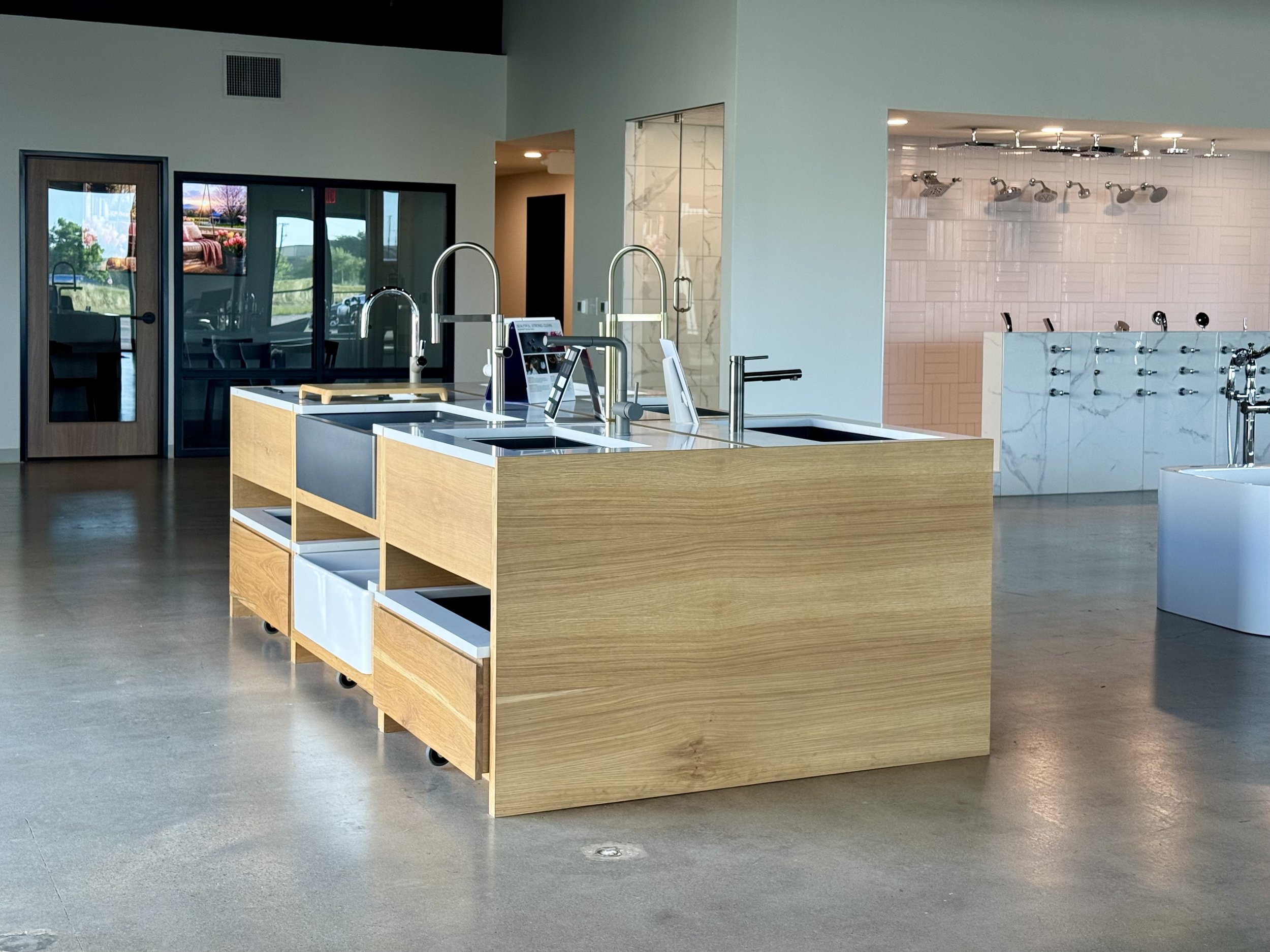 Modern interior space featuring a large island with sinks, faucets, and open storage, with a shower area visible in the background.