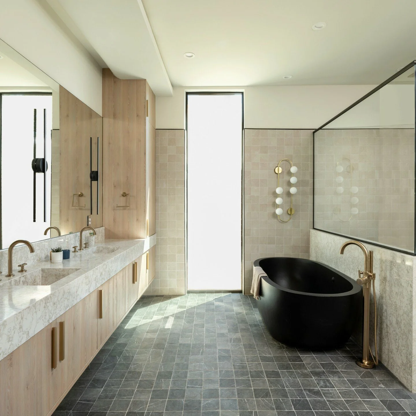 Modern bathroom with black bathtub, double sinks with marble counters, wooden cabinets, a large mirror, and a decorative wall sconce with multiple white globes.